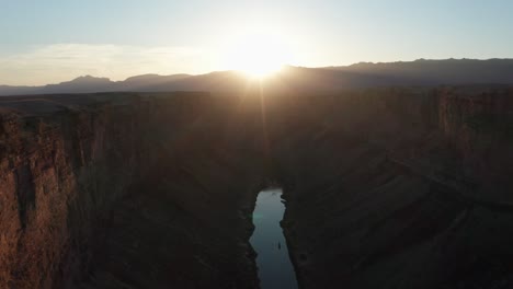 cinematic aerial shot over marble canyon, colorado river, as the sun sits at the peak of the distant mountains, creating dramatic lens flare