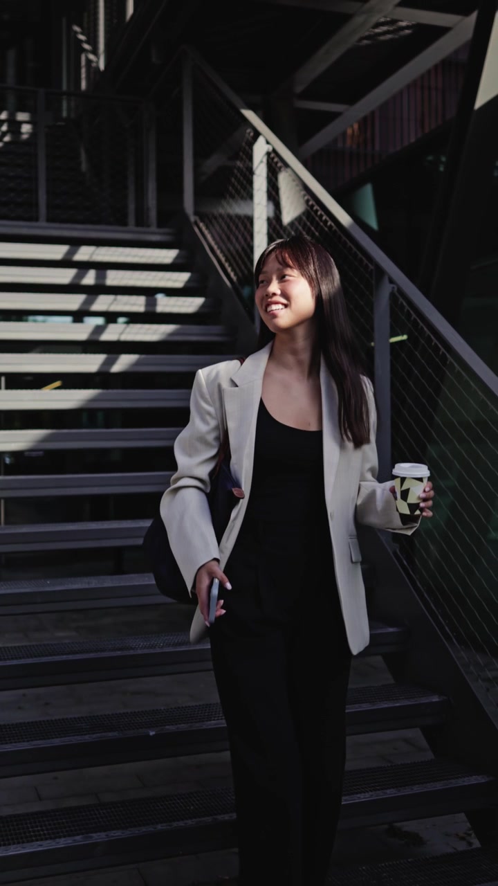 Giovane donna asiatica felice che scende le scale con caffè e smartphone