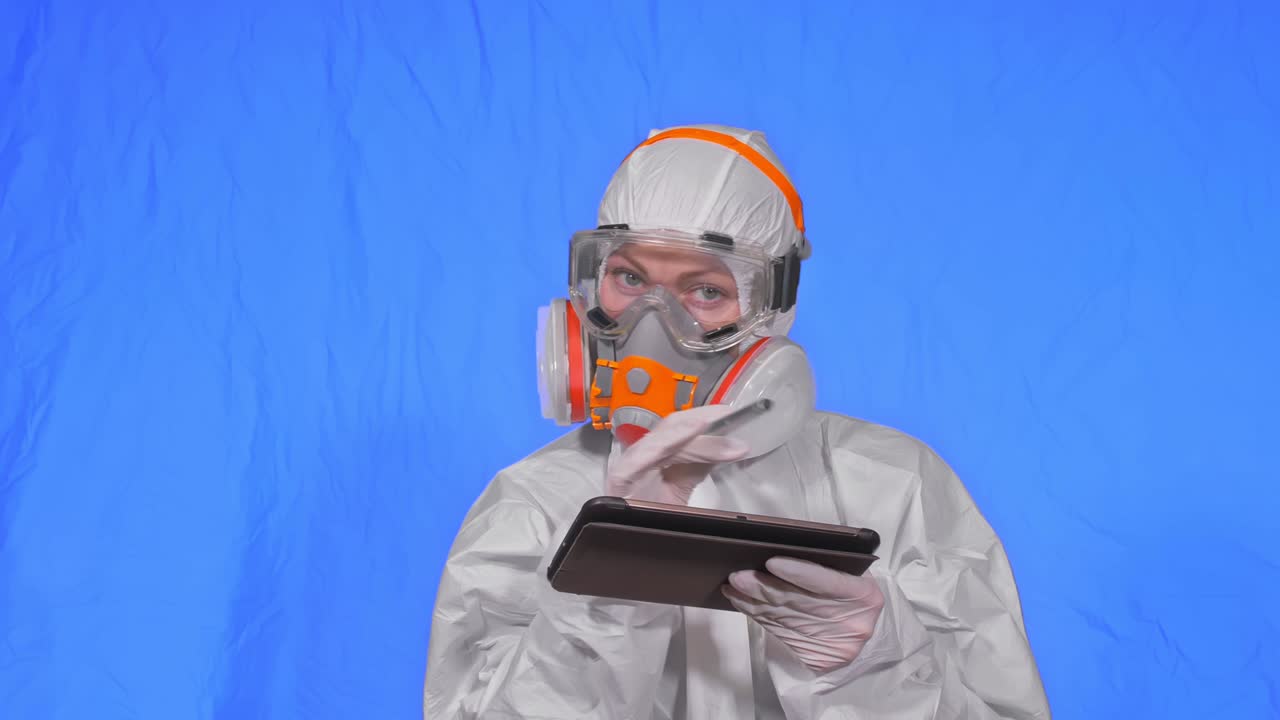 científico virólogo en respirador hace escribir en una tableta con lápiz. mujer con máscara médica de protección. clave de croma azul.