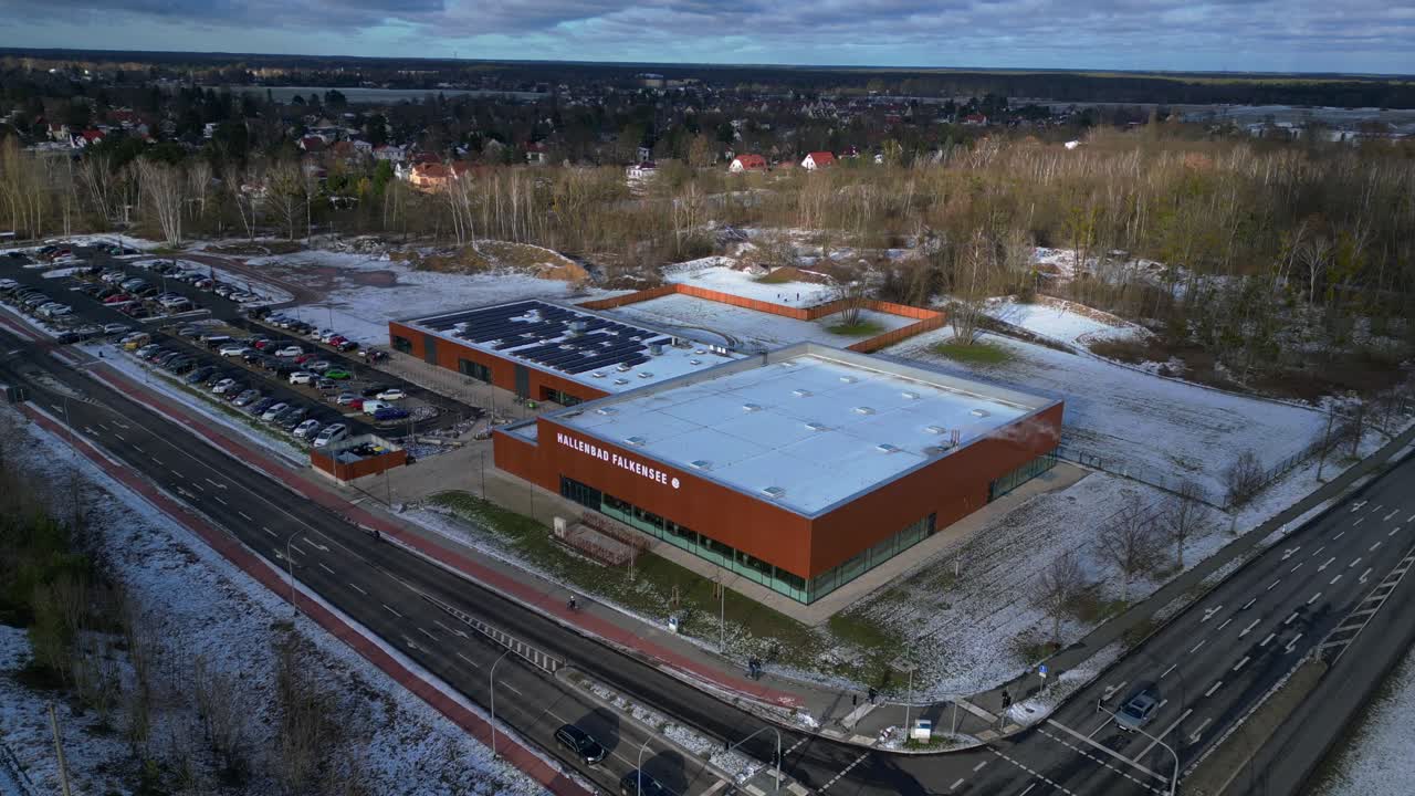 Indoor swimming pool with solar panels surrounded by snow and suburban homes in Falkensee Germany. Smooth aerial view flight drone shot footage from above