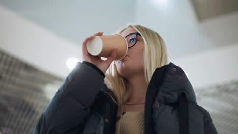 woman sipping beverage in black jacket inside a well-lit mall, captured in a close-up shot, a moment of relaxation while enjoying a drink during a visit to a modern public space