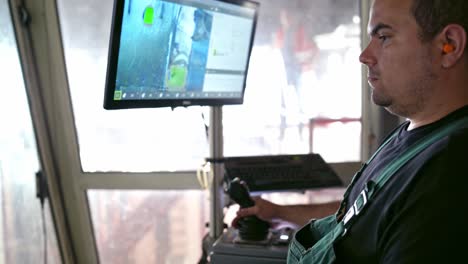 Worker at a modernized industrial factory. Man manages the robotic technologies while sitting in a room and looking at monitor.