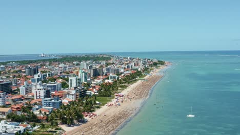 toma aérea derecha de camiones de la playa de bessa en la capital tropical joao pessoa, brasil en el estado de paraiba con lugareños y turistas disfrutando del océano y los barcos de pesca en la costa en un día de verano
