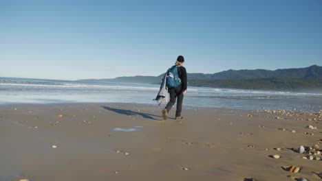 woman hiker with tripod walks on wide expansive sandy ocean beach