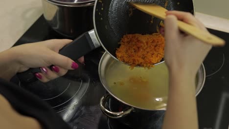 Adding-grated-carrot-into-saucepan-with-soup-with-potato-and-fish