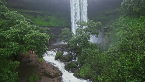 a mesmerizing panning drone view of vasudhara falls, bhandardara, maharashtra, india surrounded by lush green forests. the misty monsoon clouds create a dreamy aura 4k