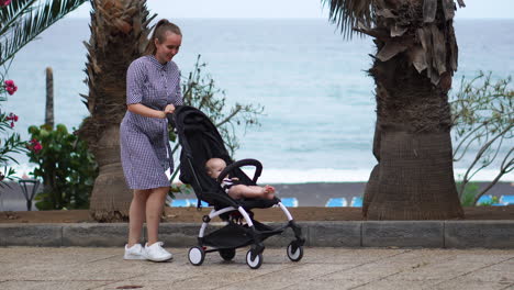 in a park filled with vibrant flowers during the summer, a young mother leisurely walks with her baby in a stroller. her contentment is palpable as she accompanies her son