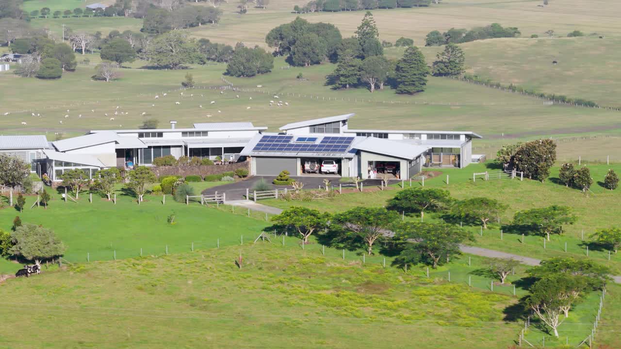 Drone footage captures a panoramic view of a modern house on lush farmland in Byron Bay under bright daylight