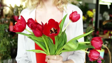 Female-florist-holding-bunch-of-red-flower-in-flower-shop