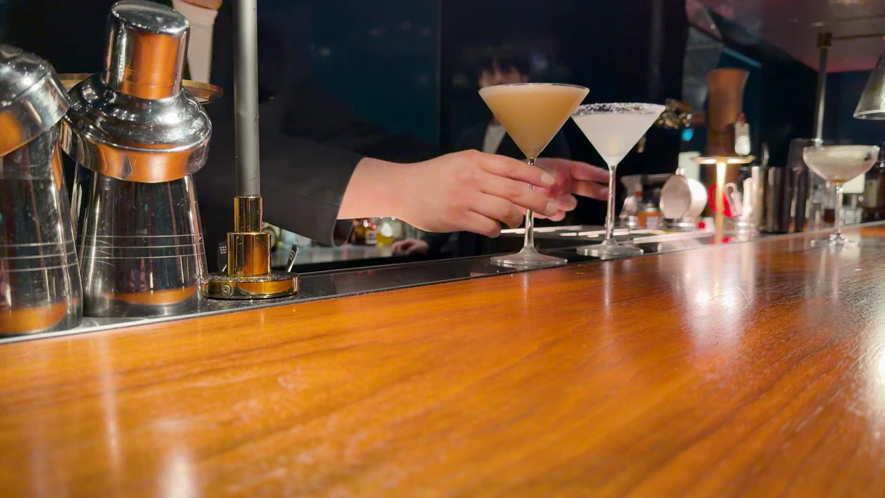 Un barista in giacca e cravatta prepara e serve un martini su un bancone di legno lucido