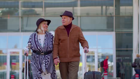 Stylish-retired-family-grandmother-grandfather-walking-with-luggage-suitcase-bags-from-airport-hall