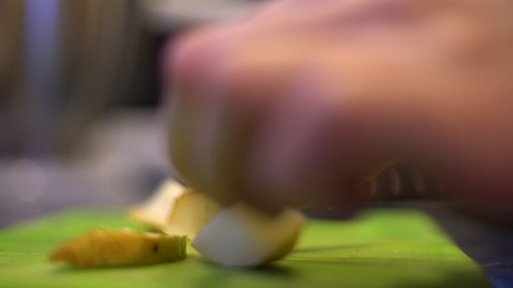 Primo piano di mani che affettano una pera su un tagliere verde