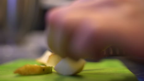 cerca de manos cortando una pera en una tabla de cortar verde