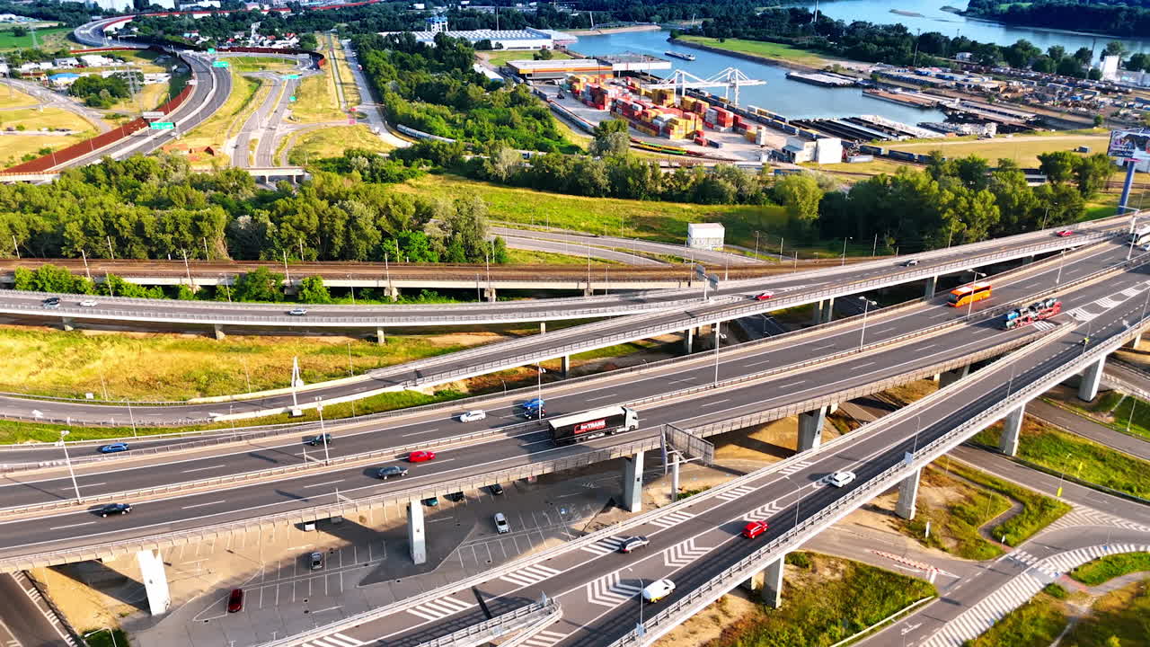 European truck-filled junction. Trucks navigate a complex highway junction near a river and industrial area during daylight, showing urban activity