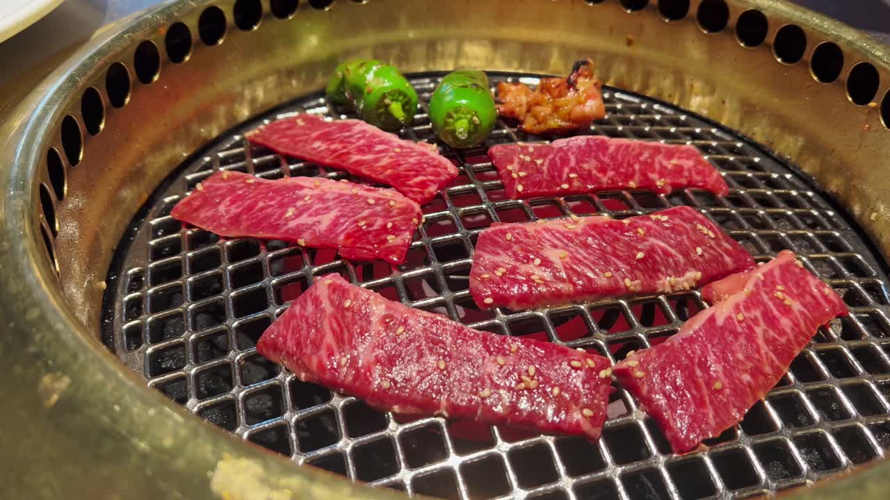Carne che sfrigola e cuoce su fiamme di carbone ardente a un barbecue in stile giapponese. Fumo e fuoco creano un'atmosfera sensoriale intensa.