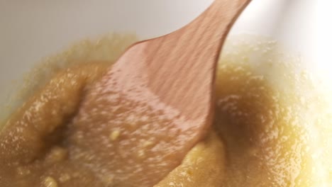 Macro-closeup-shot-of-wooden-spatula-mixing-liquid-dough-in-bowl