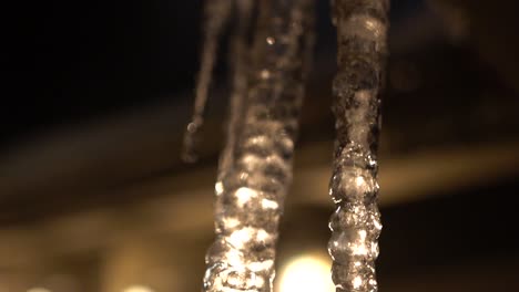 backlit melting icicle hanging from roof, dripping in slow motion, shot panning downwards