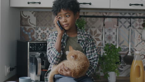 boy talking on phone while holding a cat in the kitchen