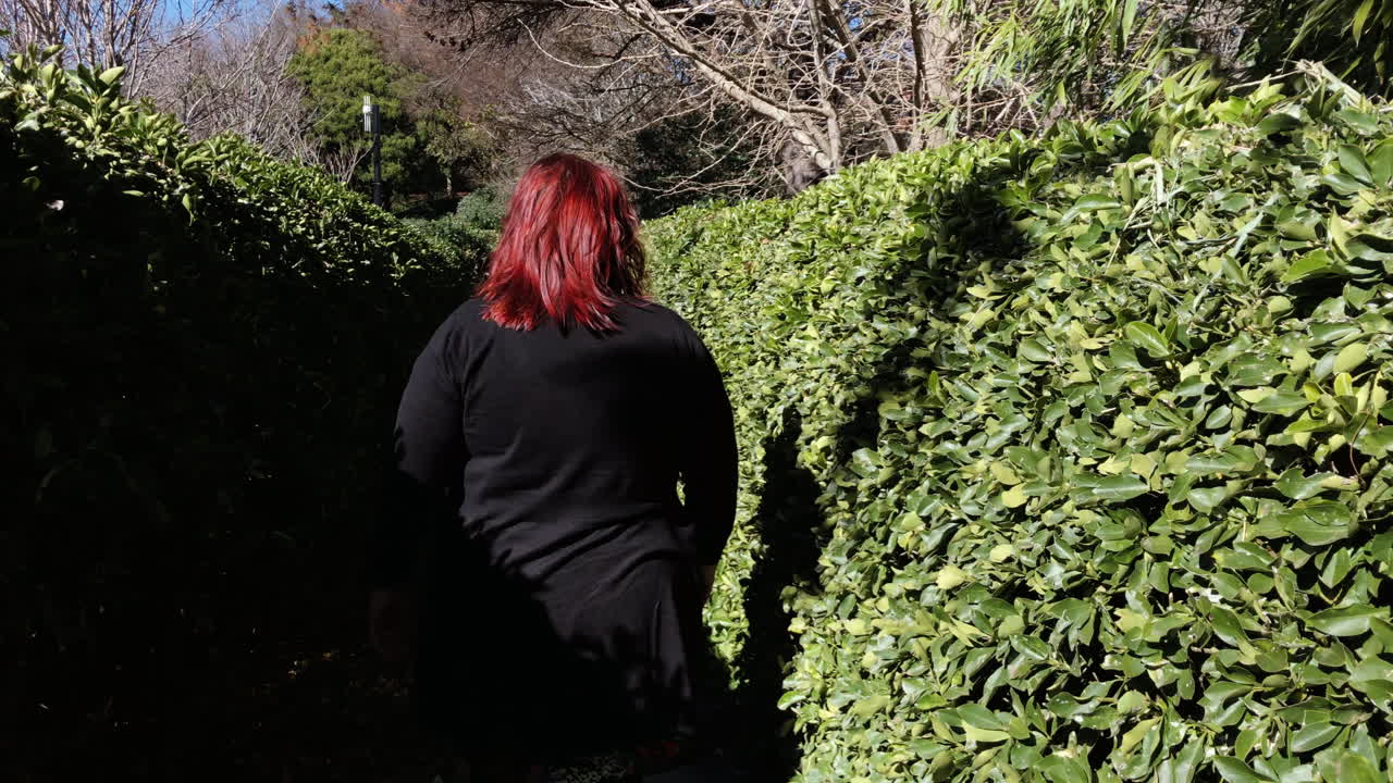 Ripresa POV al rallentatore di una donna che cammina lungo un sentiero di pietra, circondata da siepi verdi, Giardino Giapponese Ju Raku En, Toowoomba, Australia.