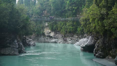 slowmo - group of people on suspension bridge above blue glacier river at hokitika gorge, new zealand