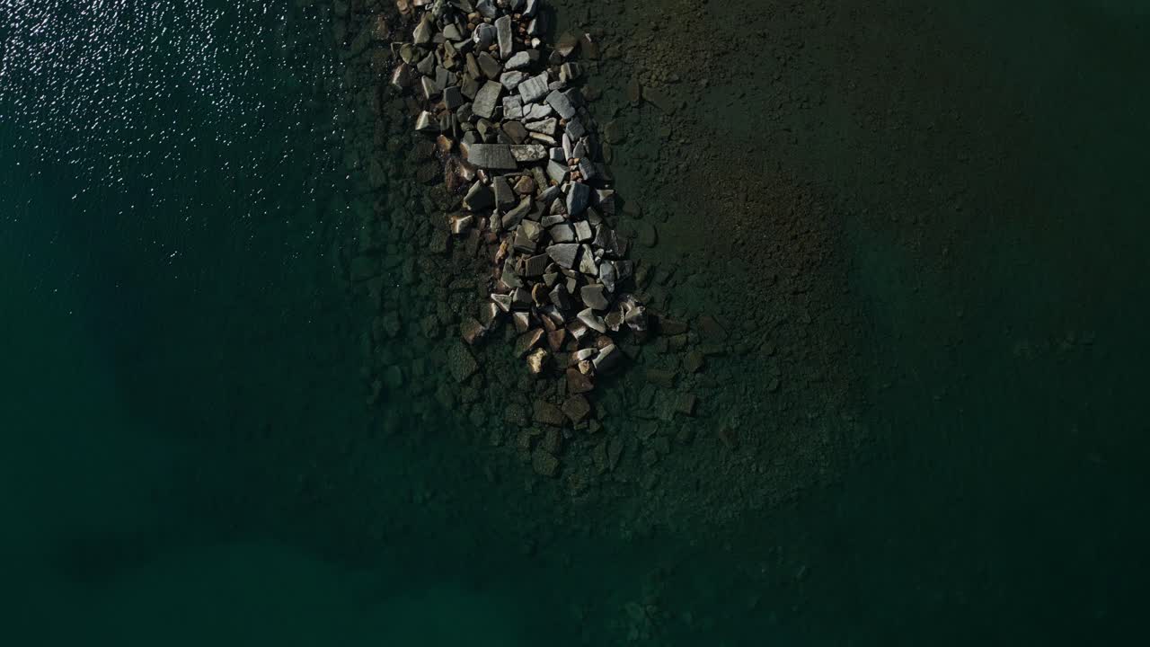 Veduta aerea rotante dall'alto sopra un frangiflutti di roccia su una spiaggia con acqua turchese