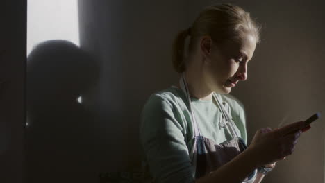 smiling woman browsing smartphone and social media while sitting by a kitchen window