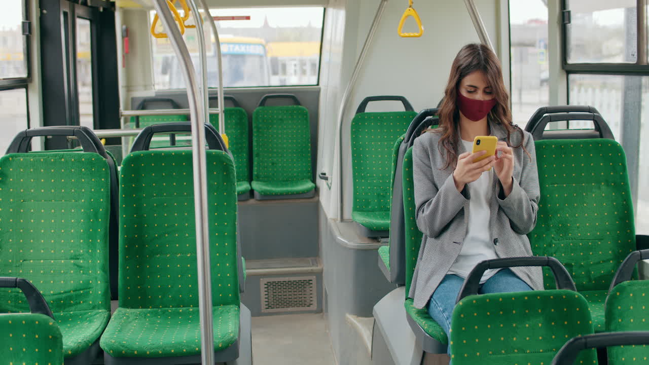 Woman wearing a face mask and using a smartphone on a bus
