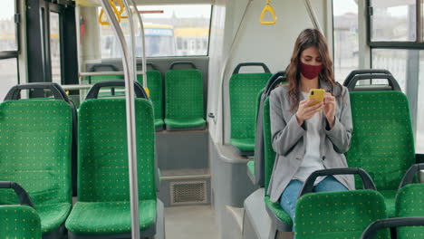 woman wearing a face mask and using a smartphone on a bus