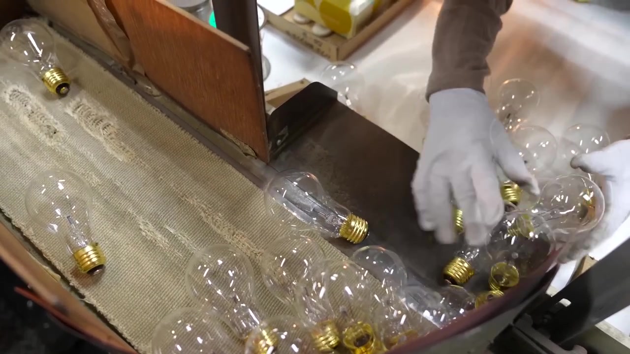 Gloved hands sorting finished incandescent bulbs with brass bases on cloth