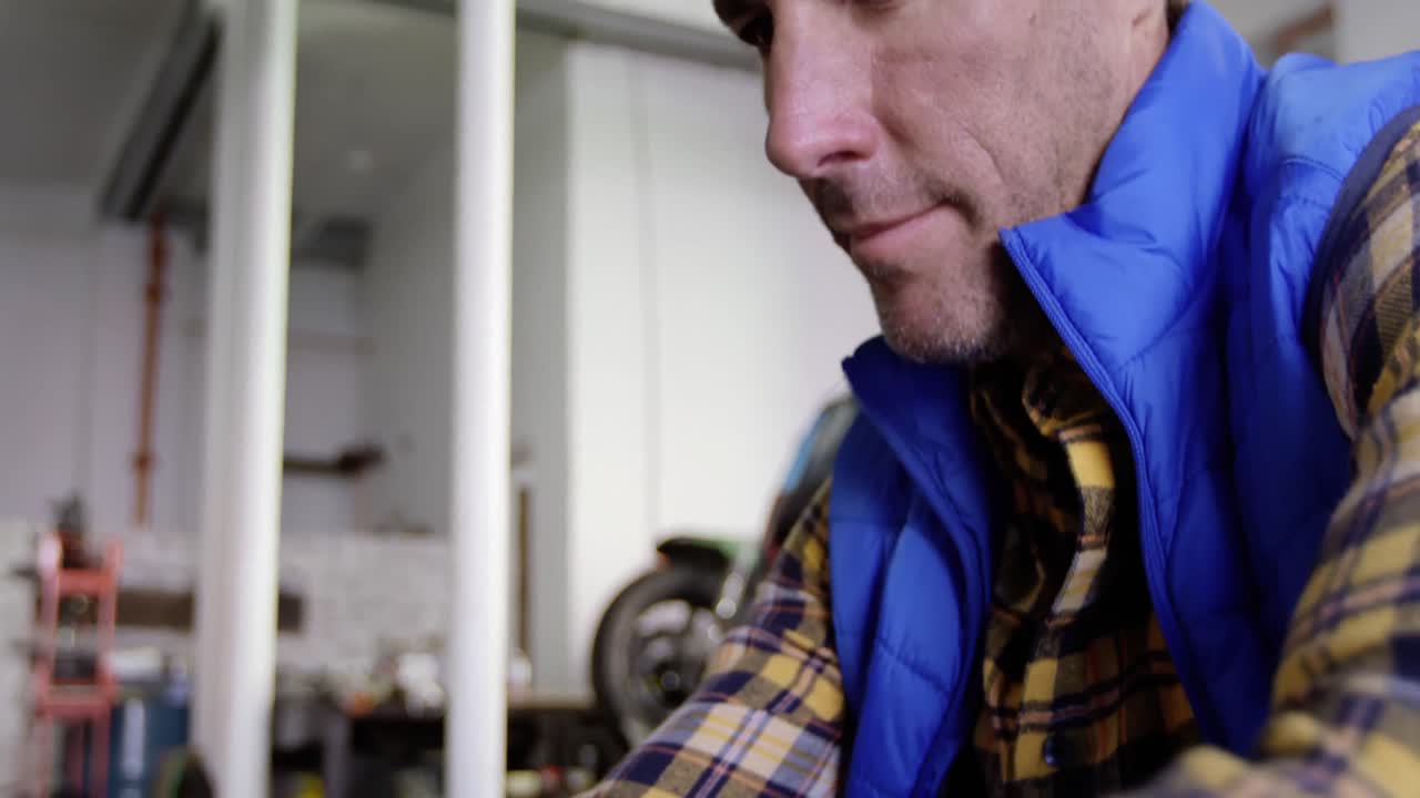 männlicher mechaniker mit mobiltelefon in einer motorradreparaturwerkstatt 4k