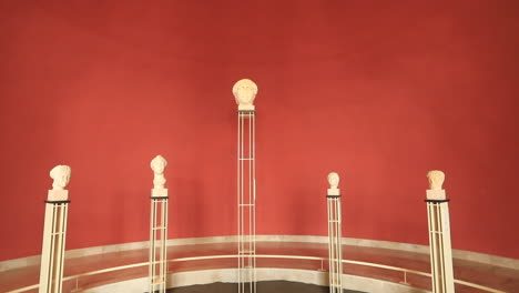 five classical busts are displayed on tall pedestals against a striking red backdrop in an art exhibit