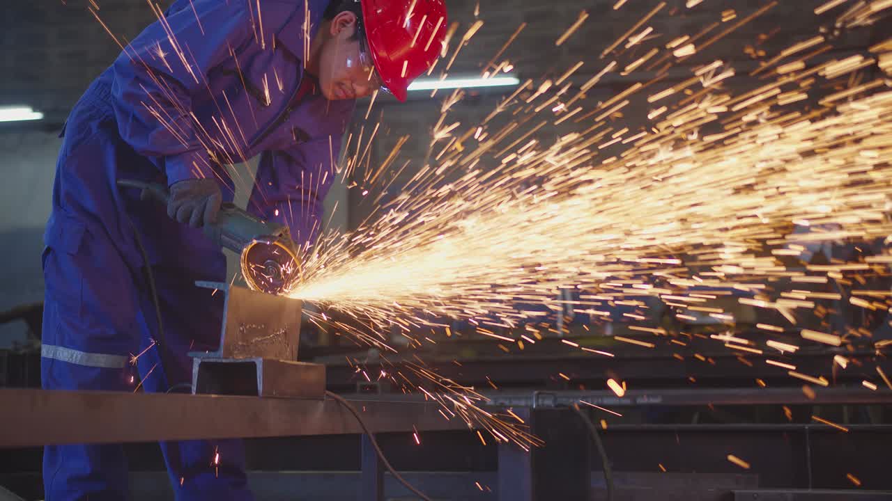 trabajador técnico masculino asiático en un uniforme seguro usar soldadores cueros, rueda eléctrica molienda en la estructura de acero en el taller de la fábrica en el garaje, chispas bokeh naranja vuelan a los lados