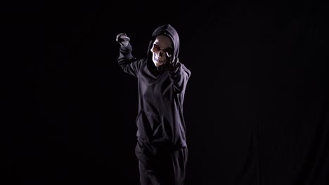 hombre aterrador en la sudadera con capucha con máscara de halloween sosteniendo un cuchillo y apuntando a la cámara mientras corre sobre el fondo negro
