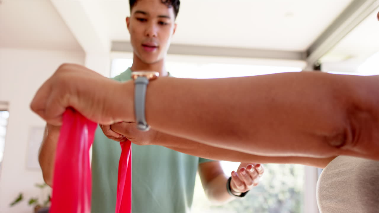 Helping senior woman with resistance band, male physiotherapist guiding exercise