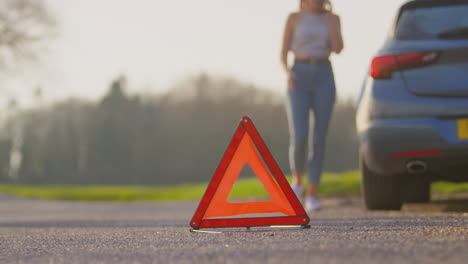 señal de triángulo de advertencia de peligro para la avería del automóvil en la carretera con una mujer pidiendo ayuda