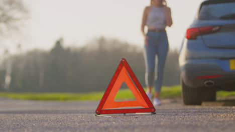 hazard warning triangle sign for car breakdown on road with woman calling for help