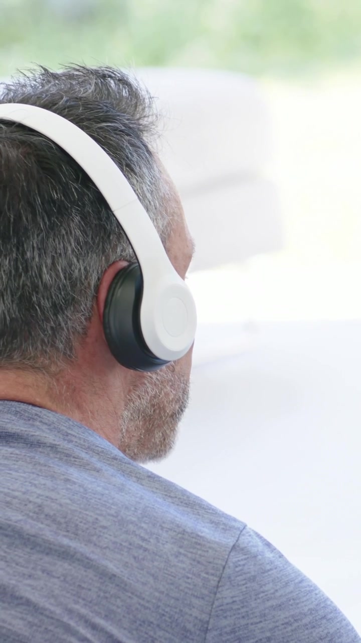 La telecamera si allontana, un uomo gira la testa verso la finestra, indossa una maglietta mélange e cuffie bianche, con spazio per il testo.