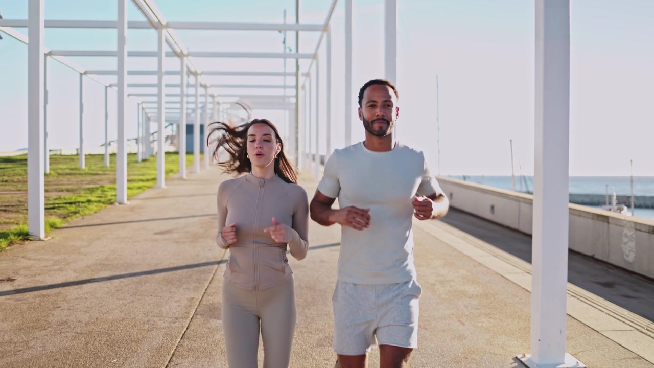 Giovane coppia che fa jogging insieme su una passeggiata lungomare soleggiata