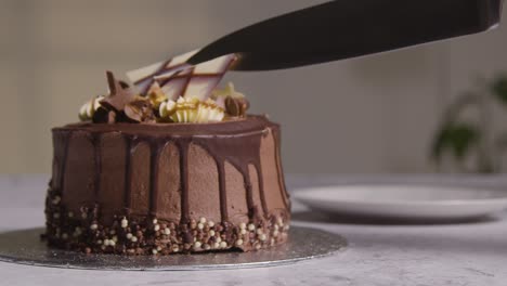 close up shot of person at home cutting slice from chocolate celebration cake on table