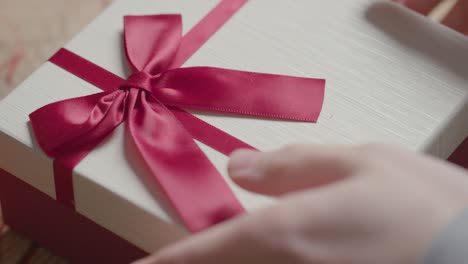 close up of man picking up romantic valentines present in gift wrapped box from table