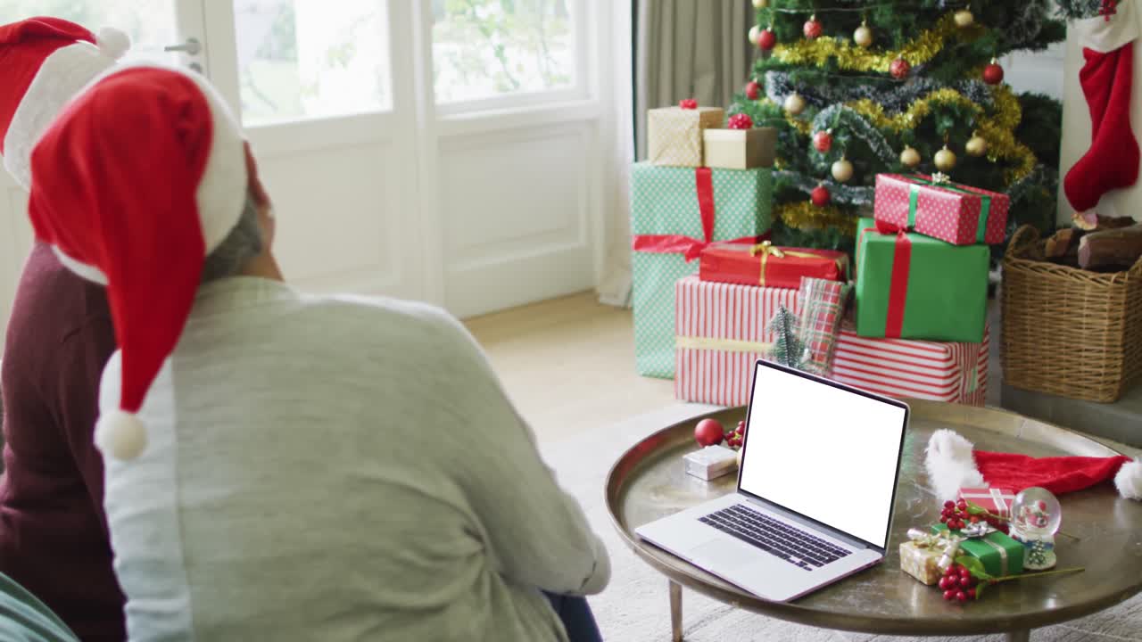 una pareja caucásica de alto nivel con sombreros de santa haciendo una llamada de video de navidad por computadora portátil, copia el espacio en la pantalla