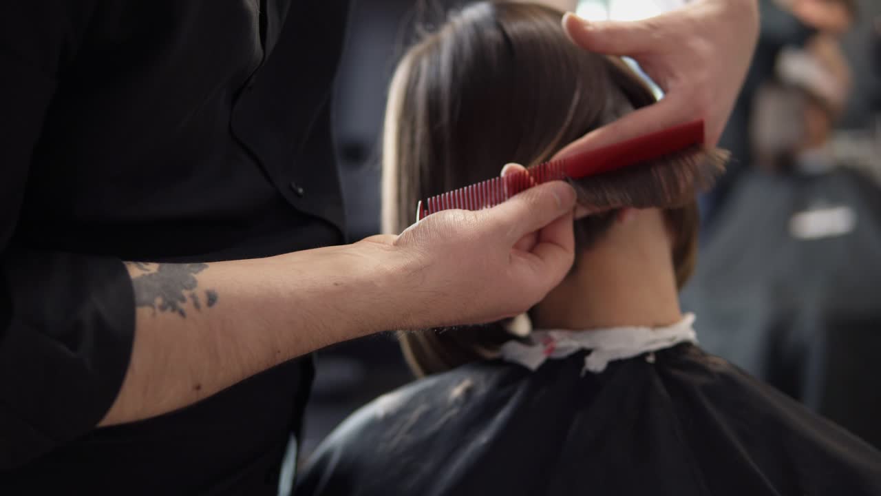 Closeup view of a barber cutting hair of young woman in professional hair salon. Beauty and haircare concept. Shot in 4k