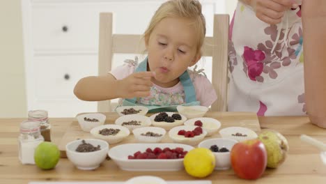 little girl placing berries on muffins