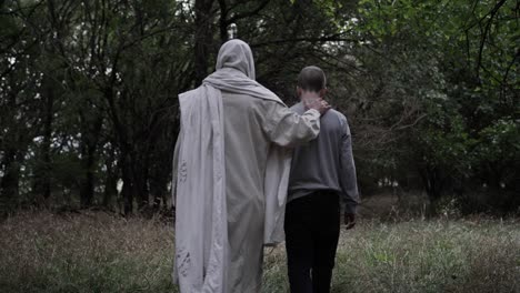 jesus walks through forest with his hand on a young teen boys back