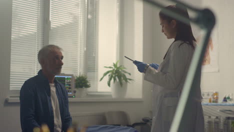 doctor consulting sick senior patient using tablet in hospital.