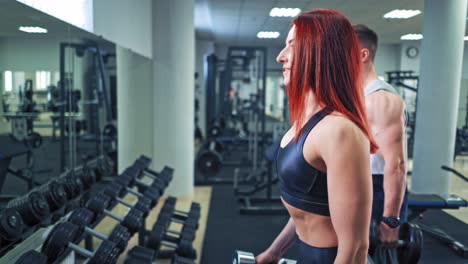 athletic man and woman during training in the sports club. hard workout of sporty couple with dumbbells on the gym background.
