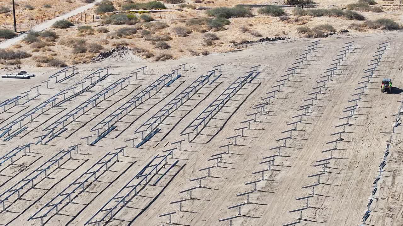 vista diurna de un sitio de construcción de paneles solares en un entorno desértico, con trabajadores y marcos metálicos.