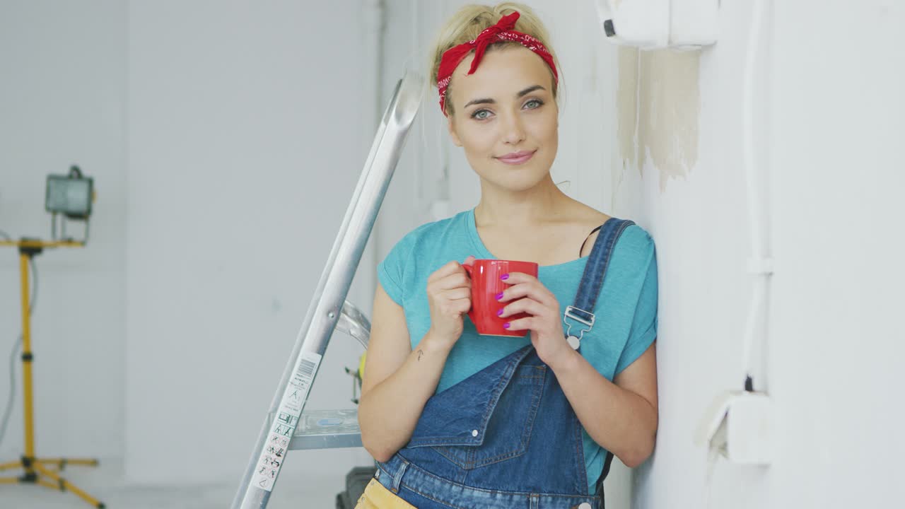 mujer sonriente en overoles apoyándose en la pared