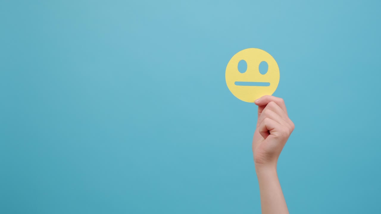 화를 내고있는 여성 손의 가까운 모습 심각한 노란 얼굴 이모티콘, 홍보 개념을 위해 복사 공간과 함께 스튜디오의 파란색 배경 벽에 고립되어 있습니다.