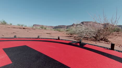 Punto-De-Vista-De-Drones-Mientras-Aterriza-En-El-Suelo-Rojo-Con-Los-Enormes-Acantilados-En-El-Fondo